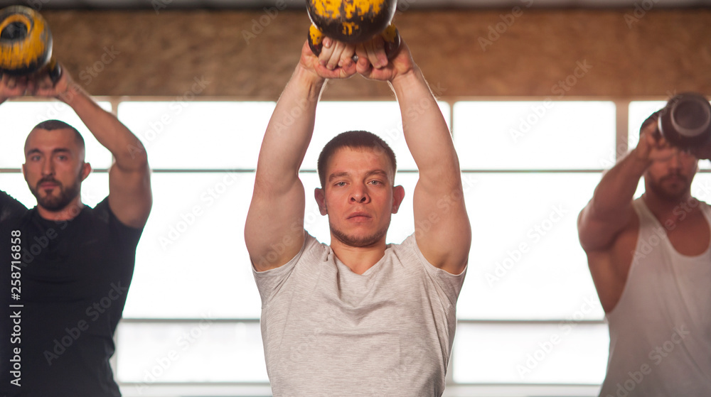Naklejka premium Multi-ethnic Group of Male Athletes Training With Kettlebells in Gym