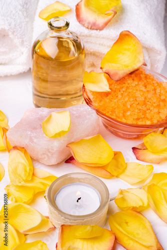 Wellness center. Composition with orange-flavored bath salts, transparent glass bottle with perfumed essential oil, white towels, rose petals and candle.