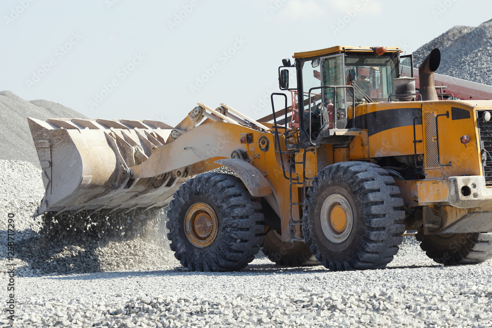 Heavy wheel loader excavator pours gravel out of the bucket, closeup. Quarry equipment. Mining industry.