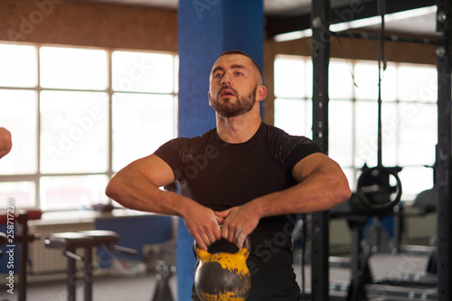 Fit And Concentrated Young Man Training With Kettlebell in Gym.
