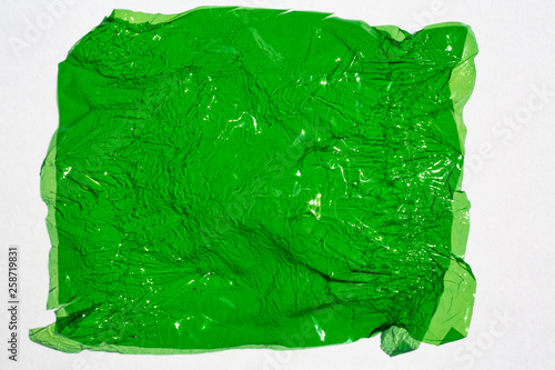 Fotografi Thin sheet of green colour cellophane with shiny crumpled surface texture  on wh