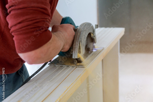 Man hands holding circular saw and preparing to make a cut wood door