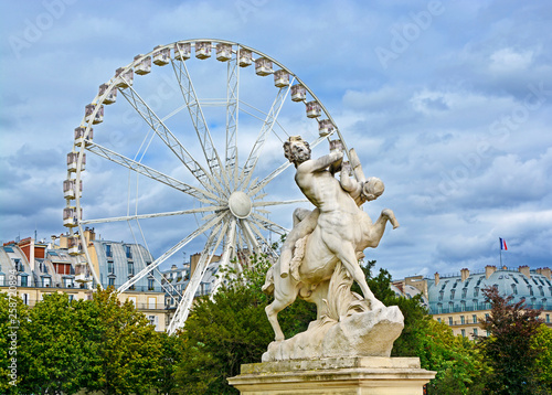 Marble statue and ferriw whell in Tuileries Garden (Jardin des Tuileries). Is public garden located between Louvre Museum and Place de la Concorde in Paris, France