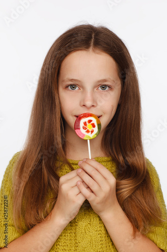 Emotional portrait of an eight-year girl in a yellow-green sweater and with a lollipop in her hands