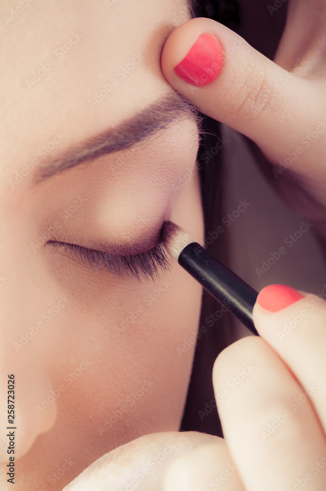 Closeup of hands applying eyeshadow powder on female facial skin