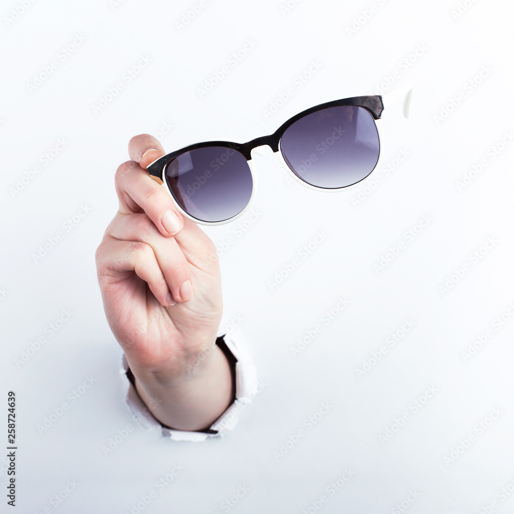 Female hand out of the hole in the paperman, holding sunglasses for vision. Isolate on white background. Female hand out of the hole in the paperman, holding sunglasses for vision. Isolate on white background.