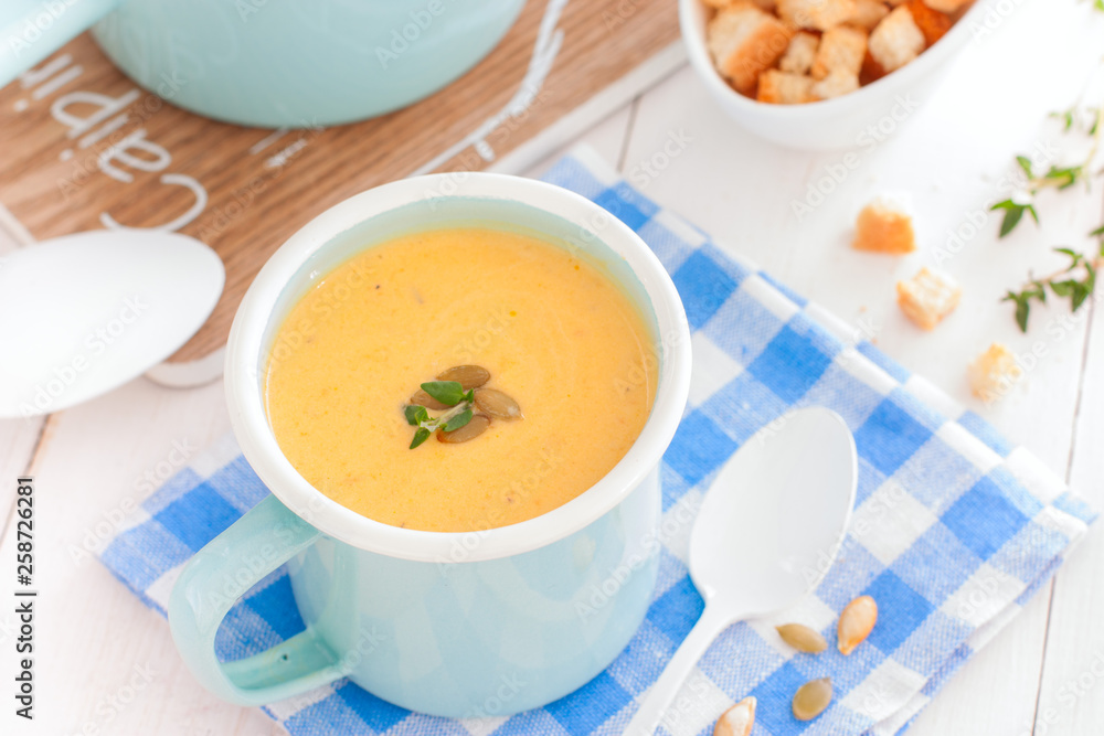 Pumpkin soup in blue enamelled mug with pumpkin seeds, horizontal Pumpkin soup in blue enamelled mug with pumpkin seeds, horizontal