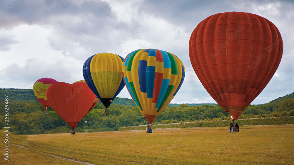 Fototapeta premium Five Hot Air Ballons Taking off in front of green hills and field