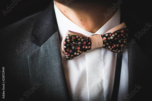 Beautiful brown bow tie with small colorful flowers on white shirt and grey jacket