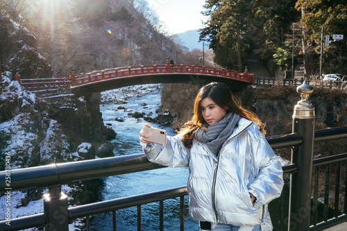 Tourist woman selfie by Smartphone with  Shinkyo Bridge, Nikko, Japan in Winter