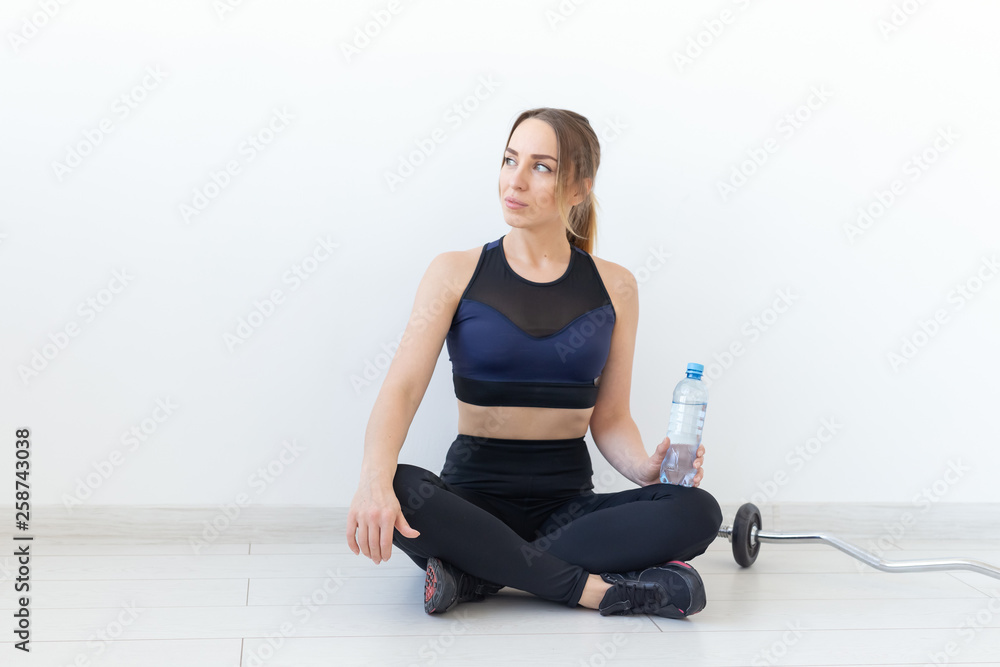 Fototapeta premium People, sport and fitness concept - young woman sitting with bottle of water on gym mat