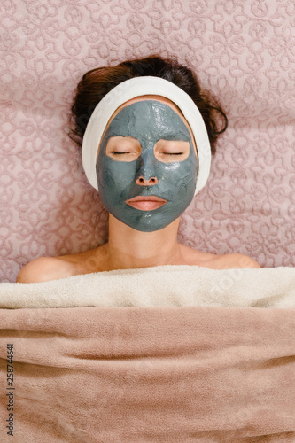 Portrait of young woman with mask on face having cosmetology treatment in spa