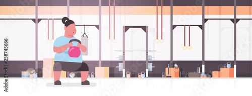 fat obese woman doing exercises with kettlebell overweight fatty girl training in gym studio workout weight loss concept flat modern health club sudio interior horizontal