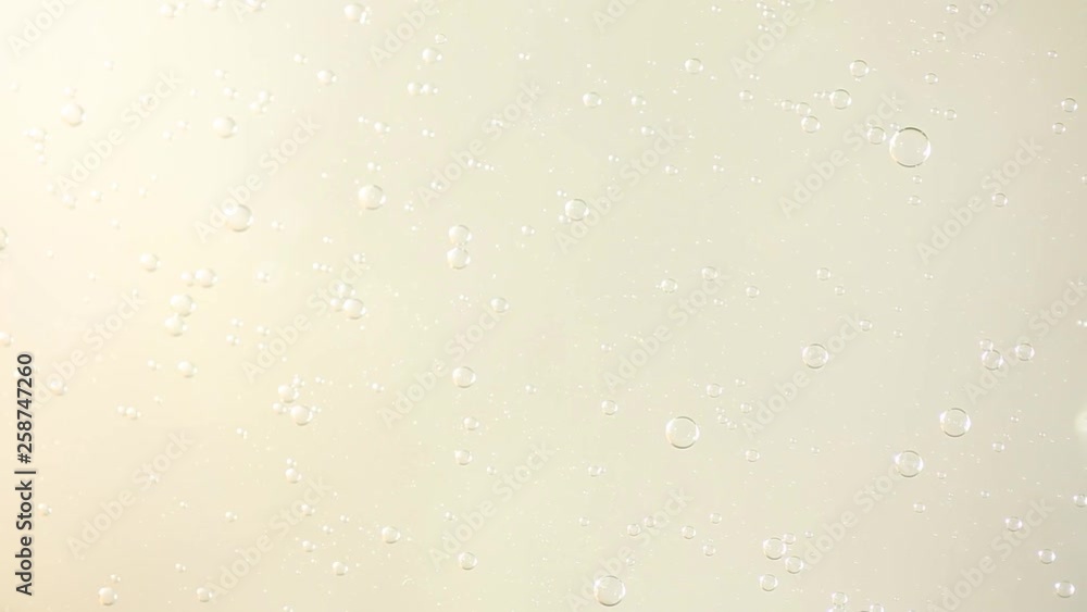 Oil and water bubbles swirl slowly over a pale yellow low contrast background Oil and water bubbles swirl slowly over a pale yellow low contrast background