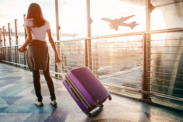 Young woman pulling suitcase in  airport terminal. Copy space