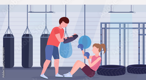sportswoman boxer doing boxing exercises with personal trainer girl fighter in blue gloves working out on floor fight clubwith punching bags gym interior healthy lifestyle concept horizontal