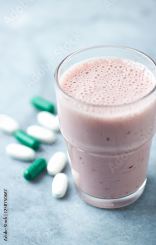 Glass of Protein Shake with milk and raspberries. BCAA amino acids and L - Carnitine capsules in background. Sport nutrition. Bright tone background. Close up. Copy space. 