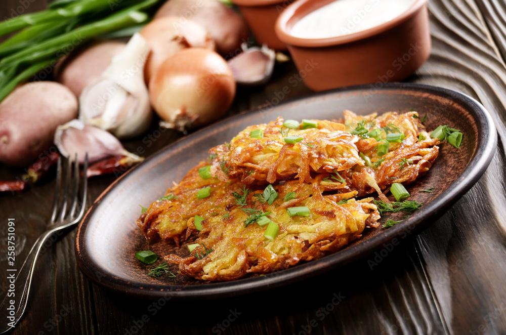 Fresh homemade tasty potato pancakes in clay dish with vegetables on wooden table