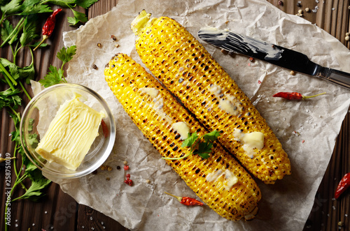 Φωτογραφία Top view of kitchen table with grilled sweet corn cob under melting butter and g