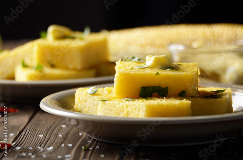 Polenta with butter and greens on clay dish on wooden rustic table