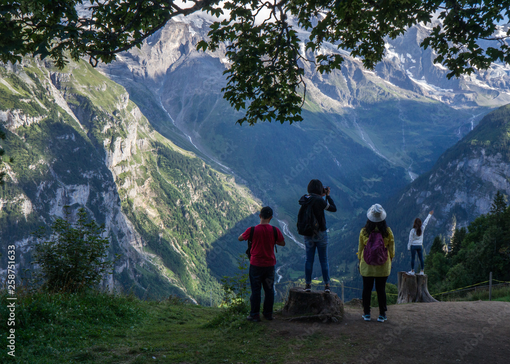 Group of people admire the mountain landscape in Muren, Switzerland. Youngest girl is pointing at a mountain while staying on a stump Group of people admire the mountain landscape in Muren, Switzerland. Youngest girl is pointing at a mountain while staying on a stump