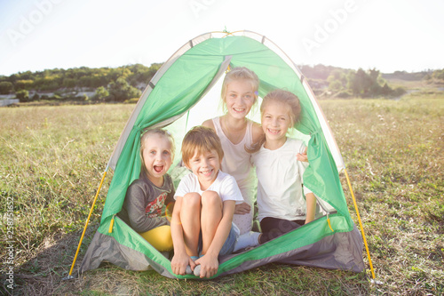 group of happy smiling children inside tent during hiking rest leisure in summer grass field