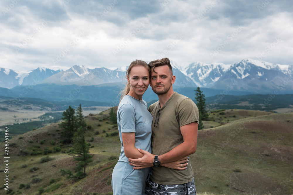 Romantic couple in the mountain, in Altai Mountains. Happy man and woman hug on the background of a mountain glacier, smiling and and look into the camera