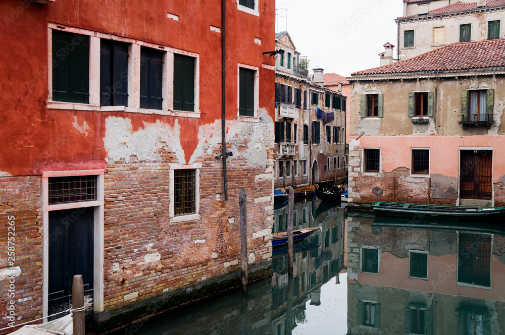 Venice canal street with houses reflecting in water with red old walls and windows 