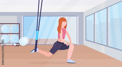 sporty woman doing squats exercises with suspension fitness straps elastic rope girl training crossfit workout concept modern gym health club studio interior horizontal full length