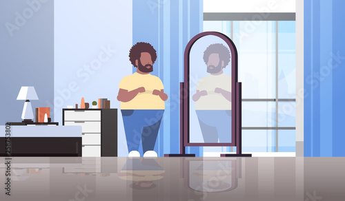 sad overweight man looking at himself reflection in mirror african american guy over size obesity concept modern apartment bedroom interior flat full length horizontal