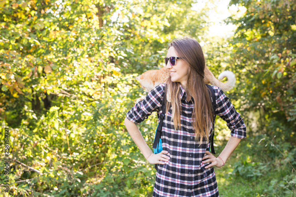 Hike, tourism and nature concept - Young female traveler with backpack and with her cat standing over forest background Hike, tourism and nature concept - Young female traveler with backpack and with her cat standing over forest background