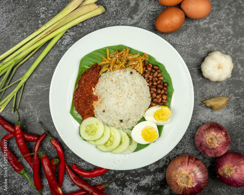 a plate of nasi lemak with ingredients on dark background. top view