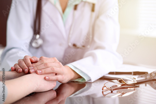 Doctor and female patient sitting at the desk and talking in clinic near window. Medicine and health care concept. Green is main color