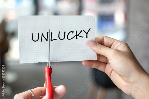 Business man hand holding red scissors and cutting white paper with the text Unlucky, change word to Lucky. challenge, positive thinking and success concept