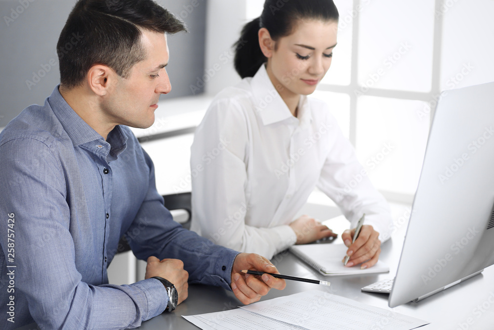 Cheerful smiling businessman and woman working with computer in modern office. Headshot at meeting or workplace. Teamwork, partnership and business concept Cheerful smiling businessman and woman working with computer in modern office. Headshot at meeting or workplace. Teamwork, partnership and business concept
