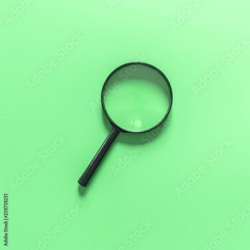 Black magnifying glass on a green background. Copy space for text