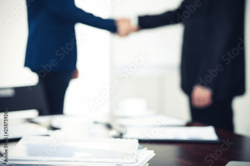 Documents and laptop on the table. Business people shaking hands on the background, silhouettes