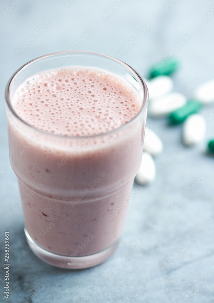 Glass of Protein Shake with milk and raspberries. BCAA amino acids and L - Carnitine capsules in background. Sport nutrition. Bright tone background. Close up. Copy space. Glass of Protein Shake with milk and raspberries. BCAA amino acids and L - Carnitine capsules in background. Sport nutrition. Bright tone background. Close up. Copy space.