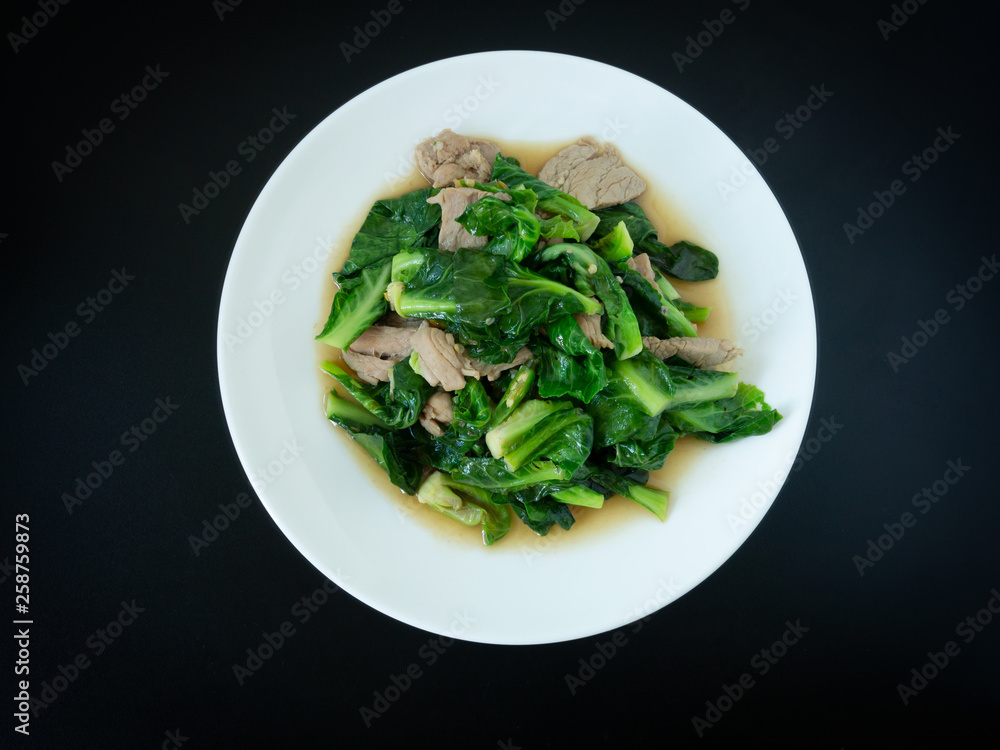 Kale fried with pork in oyster sauce menu on white plate for meal with black background. Thai food.