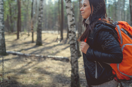 Woman with backpack walking in woods Side view of casual woman carrying backpack and walking in sunny spring woods