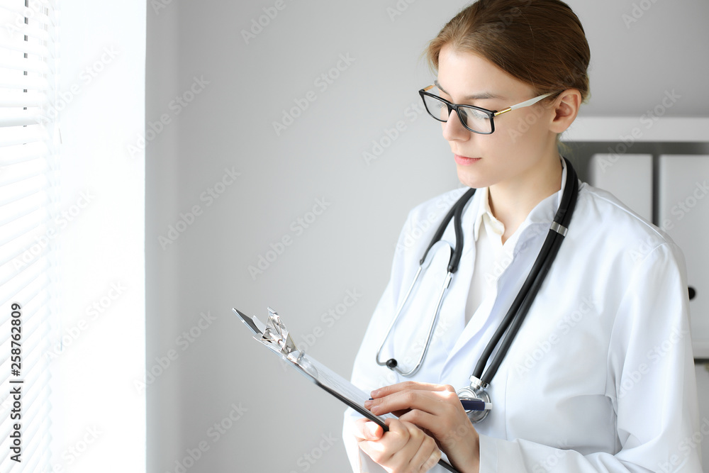 Doctor woman at work. Portrait of female physician using clipboard at hospital office. Medicine and healthcare concept Doctor woman at work. Portrait of female physician using clipboard at hospital office. Medicine and healthcare concept