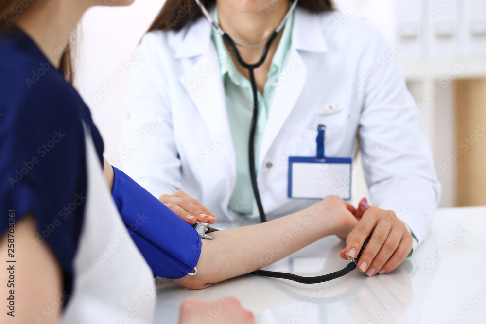 Unknown doctor woman checking blood pressure of female patient, close-up. Cardiology in medicine and health care concept Unknown doctor woman checking blood pressure of female patient, close-up. Cardiology in medicine and health care concept