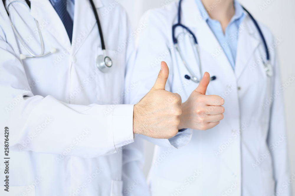Team of unknown medicine doctors showing OK sign with thumb up close up. Success and high level service in health care, best treatment and customer loyalty and physical concept Team of unknown medicine doctors showing OK sign with thumb up close up. Success and high level service in health care, best treatment and customer loyalty and physical concept