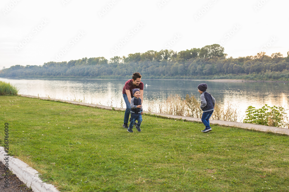 Childhood, family concept - father playing with two sons near the lake Childhood, family concept - father playing with two sons near the lake