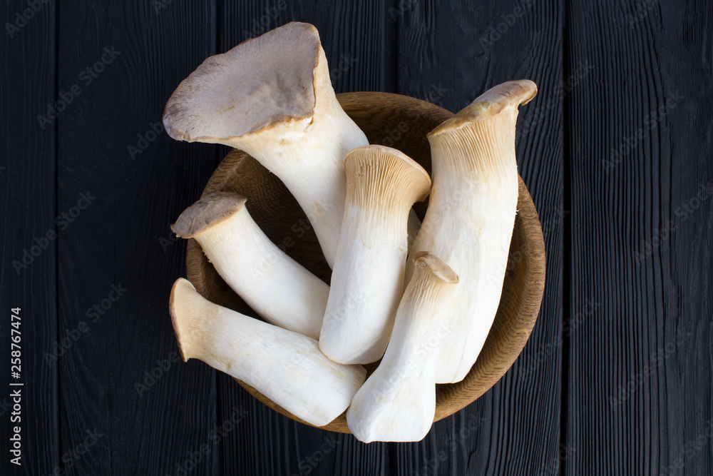 Fototapeta premium Mushrooms eringi in the brown bowl on the black wooden background.Top view.Closeup.