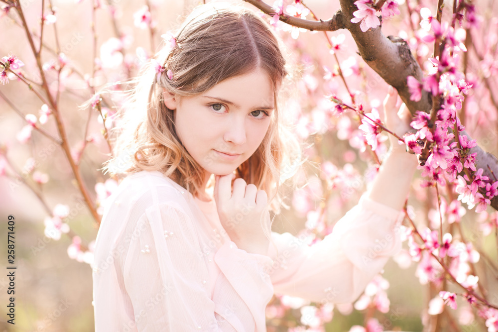 Blonde teenage girl 14-15 year old posing in peach orchard close up. Looking at camera. Spring season.