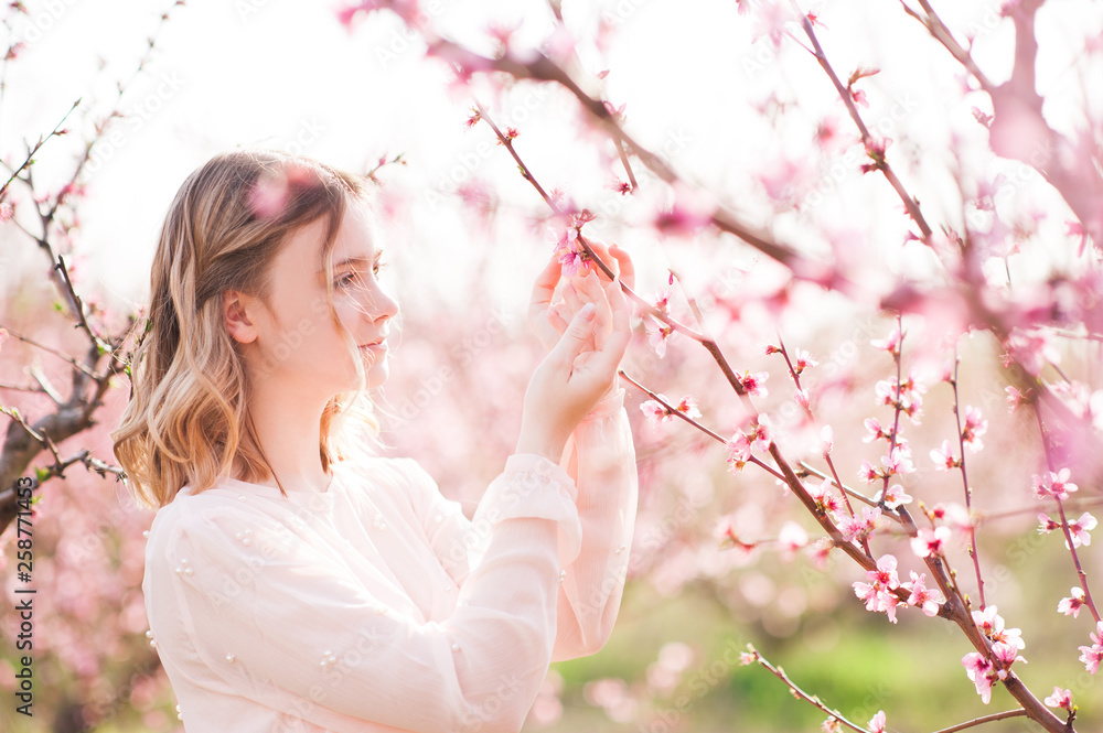Beautiful blonde teen girl 15-16 year old posing in peach orchard close up. Spring season.
