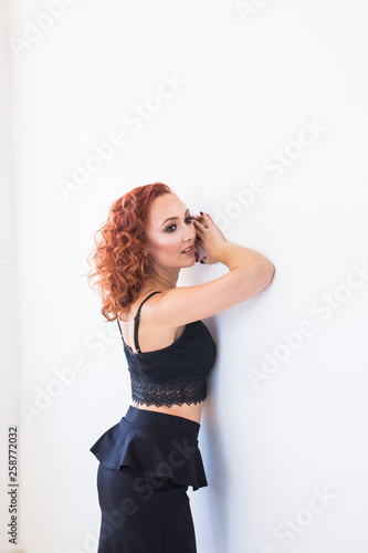 People and fashion concept - Redhead woman in black shirt and skirt posing isolated on white background