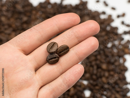 Three grains of coffee on the palm against the background of scattered coffee
