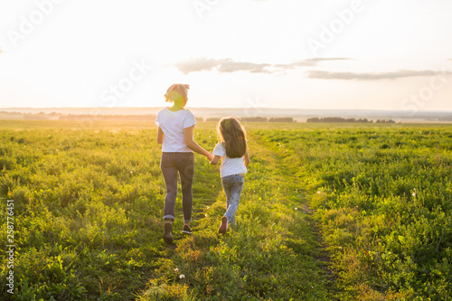 Rear view of mother and daughter running in green field with sunset on background © satura_